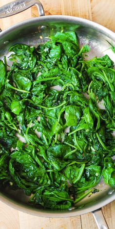 spinach and onions cooking in a pan on a wooden table with utensils