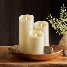 three white candles sitting on top of a wooden tray