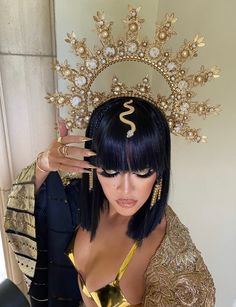 a woman with black hair wearing a gold dress and holding her hand up in front of her face