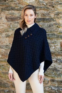 a woman standing in front of a stone wall wearing a black ponchy with buttons