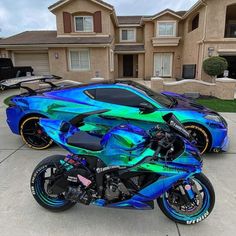 a blue and green motorcycle parked in front of a house with two cars behind it