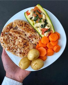 a white plate topped with meat, potatoes and veggies next to a cucumber