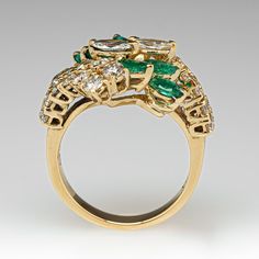 This pretty ring is centered with a cluster of two (2), prong set, marquise brilliant cut diamonds and six (6), prong set, marquise mixed cut natural emeralds. The top face of the by-pass style shank is accented with twenty-six (26), prong set, round brilliant cut diamonds. The ring measures 18.0mm at the top, rises 8.0mm above the finger, tapering to 2.9mm wide and 1.1mm thick at the base of the shank. This ring is currently a size 7. Marquise Brilliant Cut Emerald Ring, Marquise Emerald Ring With Brilliant Cut, Luxury Multi-stone Marquise Cut Diamond Ring, Luxury Marquise Cut Multi-stone Diamond Ring, Elegant Marquise Cut Multi-stone Cluster Ring, Luxury Marquise Emerald Ring With Prong Setting, Marquise Emerald Ring For Formal Occasions, Marquise Emerald Diamond Ring With Brilliant Cut, Formal Marquise Emerald Ring With Brilliant Cut