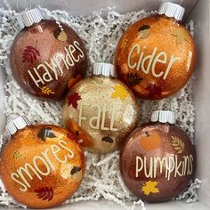 four orange and gold ornaments in a white box with writing on them that says,