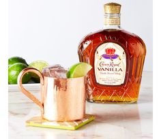 a bottle of vanilla syrup next to a copper mug filled with ice and limes