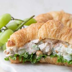 a croissant sandwich with chicken salad on it next to grapes and green beans