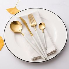 a white plate topped with gold colored utensils and napkins next to yellow leaves