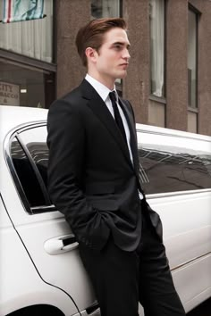 a man in a suit leaning against the side of a car