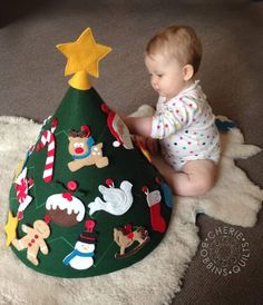 a baby is sitting on the floor next to a christmas tree shaped hat with gingerbreads and other holiday decorations