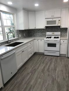 an empty kitchen with white cabinets and wood flooring