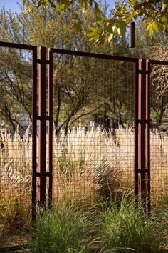 the fence is made of metal and has grass growing on it in front of some trees