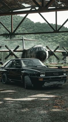 an old car is parked under a hanger with a large airplane in the background