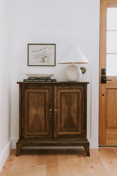 a wooden cabinet sitting next to a lamp on top of a hard wood floor