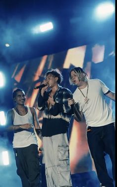 three men standing on stage singing into microphones