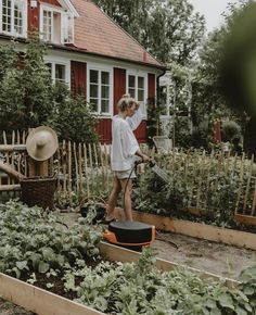 a woman watering her garden in front of a house