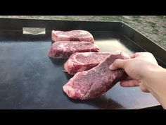 some raw meat is being cooked on a grill with someone's hand over it