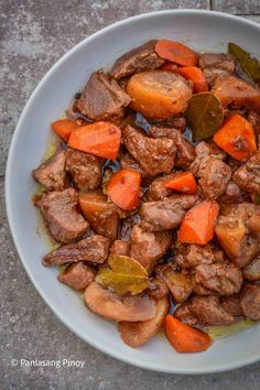 a white plate topped with meat and carrots on top of a cement floor next to a sidewalk