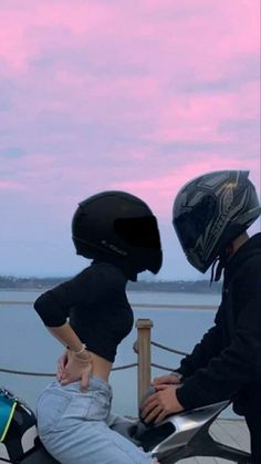 two people sitting on a motorcycle with their helmets on and one person wearing a helmet