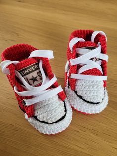 a pair of red and white crocheted shoes sitting on top of a wooden table