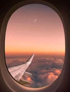 an airplane window with the view of clouds and a crescent moon in the sky above