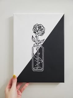 a hand holding up a black and white painting with a rose in a glass vase