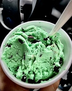 a hand holding a bowl filled with green ice cream