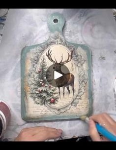 someone is painting a deer on a cutting board with holly wreaths and pine cones