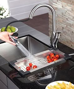 a person washing tomatoes in a kitchen sink with a faucet over the sink