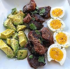 a white plate topped with steak, eggs and avocado on top of it