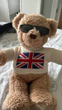 a brown teddy bear wearing sunglasses on top of a bed