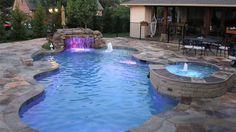 an outdoor pool with waterfall and fire pit in the middle, surrounded by patio furniture