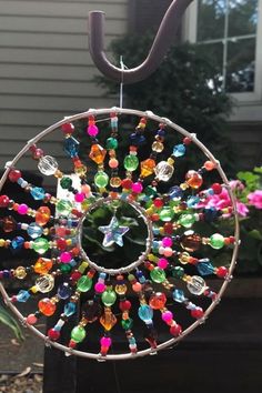 a colorful wind chime hanging from a metal pole in front of a house with flowers