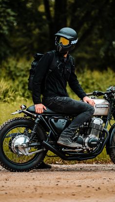 a man sitting on top of a motorcycle in front of some trees and dirt road