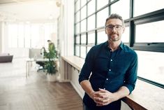 a man standing in an office with his arms crossed and looking at the camera while wearing glasses