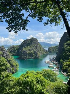 boats are docked on the water near some mountains and trees in the foreground, surrounded by lush green foliage