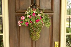 a hanging basket filled with pink and white flowers next to a brown front door handle