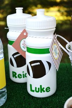 three sports themed water bottles sitting on top of a green grass covered field next to plastic cups