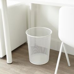 a white plastic trash can sitting next to a table and chair in a room with wood flooring