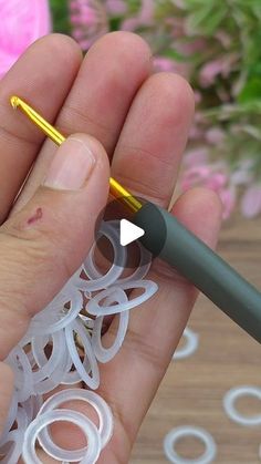 a person holding a pen in their hand with some rubber bands around it and flowers in the background