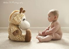 a baby sitting on the floor next to a stuffed giraffe and looking at it