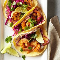 three tacos with shrimp, cabbage and cilantro on a white platter