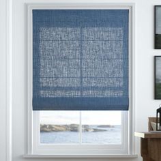 a blue roman blind in a white room with water and pictures on the wall behind it