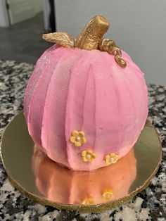 a pink cake with gold decorations sitting on top of a plate in the shape of a pumpkin