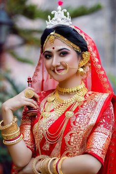 a woman in a red and gold bridal outfit posing for the camera with her hand on her hip