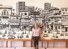 a woman sitting on top of a bench in front of a wall with a cityscape