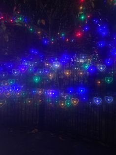 a fence covered in lots of heart shaped lights next to a forest filled with trees