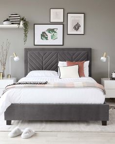 a bedroom with grey walls and white bedding, pictures on the wall above it