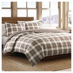 a bed with plaid comforter and pillows in front of a window on a rug