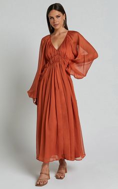 Step out in style and turn heads wherever you go with our stunning Roxanna Maxi Dress! This gorgeous A-line dress features a flattering ruched waist that cinches in your figure, giving you an effortlessly chic look. Made from luxurious georgette polyester fabric, this rust-colored beauty is perfect for any occasion - be it a party day or a special night out. The long sleeves add an elegant touch while the plunging neckline adds a hint of allure. Embrace your unique style and radiate confidence w Rust Bridesmaid Dress With Sleeves, Mission Fits, Bestie Hangout, Terracotta Dress, Boho Wardrobe, Rust Color Dress, Tudor Period, Dress Georgette, Ruched Waist Dress