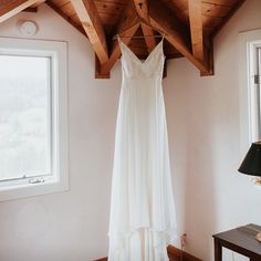 a wedding dress hanging on a wooden hanger in a room next to a window